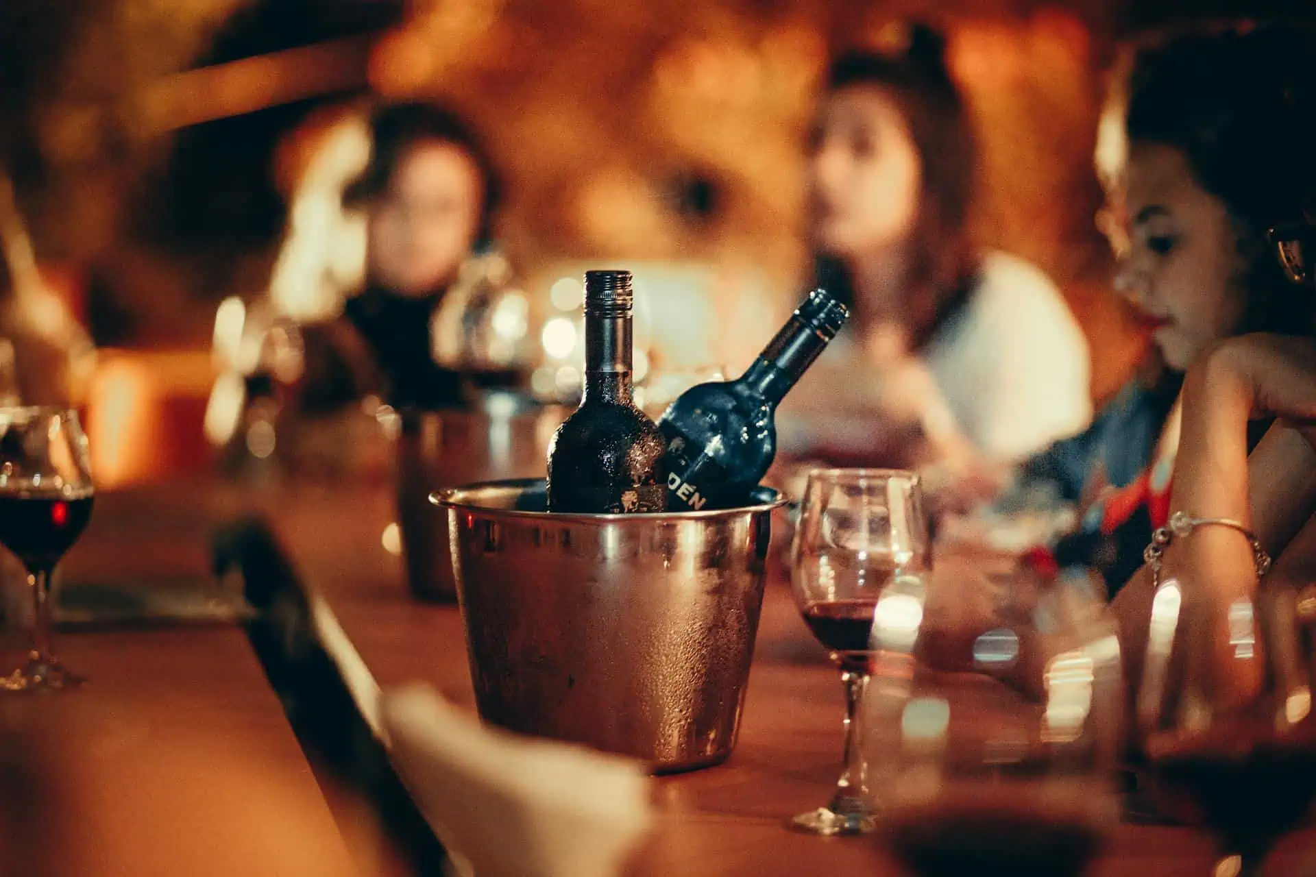 Wine bottles in an ice bucket with glasses on a dinner table.