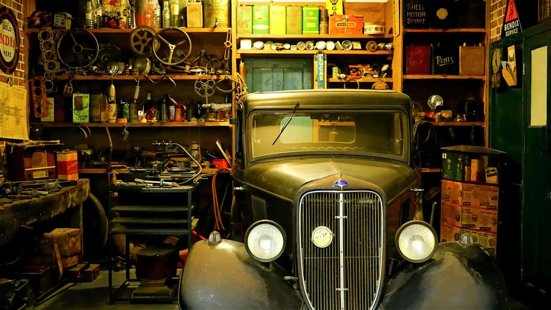 Vintage car parked inside an old, cluttered workshop with tools and shelves.