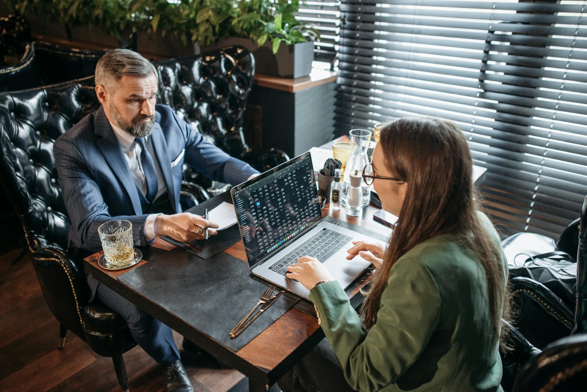 Businessman and woman having a serious discussion with laptop and drink.