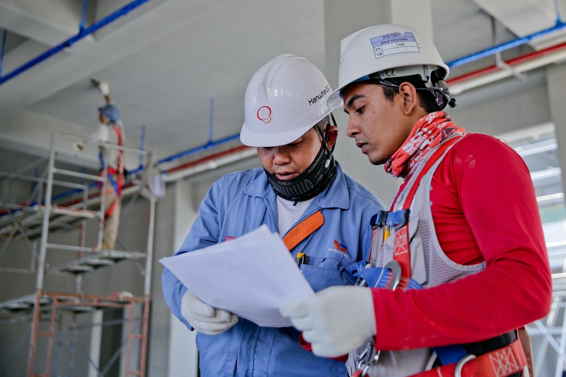 Two construction workers in safety gear examining blueprints on-site.